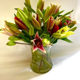 Glass vase of pink and red lilies with many green buds against a light background