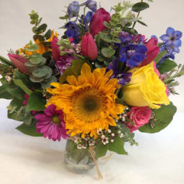 Mixed bouquet with sunflowers, roses, and blue flowers in a glass vase