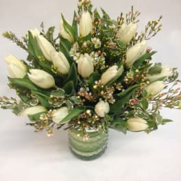 White tulips arranged in a green glass vase with small filler flowers