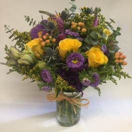 Bright yellow roses and purple asters arranged with berries in a mason jar tied with raffia
