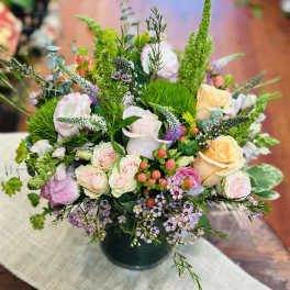 Mixed bouquet of pastel roses and small purple flowers in a dark vase