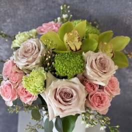 Arrangement of blush and pink roses, green orchids, and green mums in a white vase