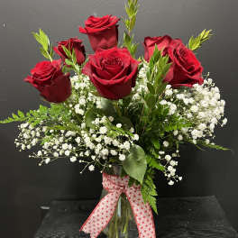 Red roses in a clear glass vase with baby's breath and a ribbon