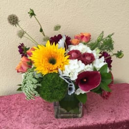 Mixed bouquet in a clear square vase with a large yellow bloom and burgundy flowers