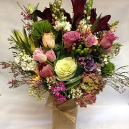 Mixed bouquet with lilies, roses, tulips, and hydrangea in a burlap-wrapped vase