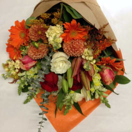 Mixed bouquet with orange daisies, roses, and lilies wrapped in brown paper