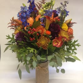 Colorful mixed bouquet with lilies, calla lilies, and chrysanthemums in a burlap-wrapped vase