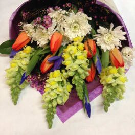 Bouquet of white daisies, orange tulips, and yellow snapdragons wrapped in purple paper