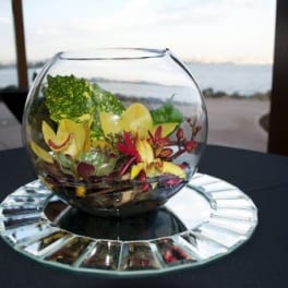 Glass bowl with yellow orchids and red flowers on a mirrored base