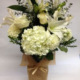 White lilies and hydrangeas arranged in a burlap-wrapped vase
