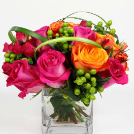 Pink and orange roses in a clear square vase with green berries
