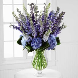 Tall blue and purple floral arrangement in a clear glass vase