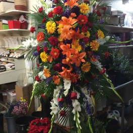 Large standing floral spray with lilies, roses, and daisies in bright mixed colors