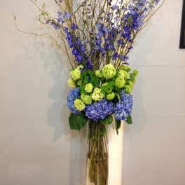 Tall blue and green floral arrangement in a clear glass vase