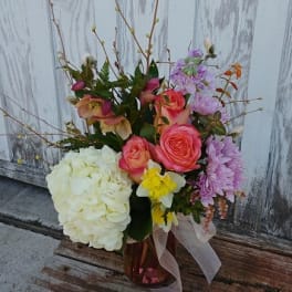 Mixed bouquet with roses, hydrangea, and daffodils in a glass vase