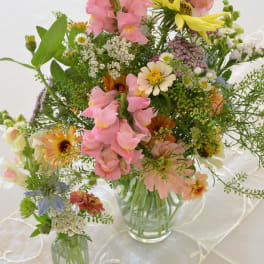 Mixed pastel flower arrangements in clear glass vases on a white tablecloth
