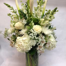 White floral arrangement in a clear glass vase with tall calla lilies and roses