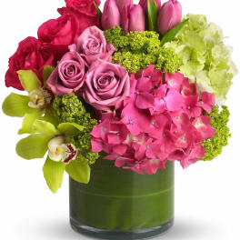 Mixed bouquet of pink roses, tulips, hydrangea, and orchids in a glass vase