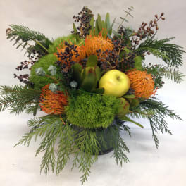 Mixed floral arrangement with orange blooms and a yellow apple in a black container