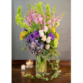 Tall mixed bouquet in a glass vase with candles beside it