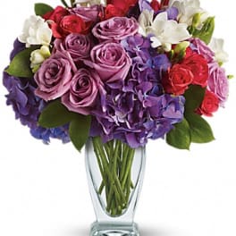 Bouquet of purple and red roses with white flowers in a clear glass vase