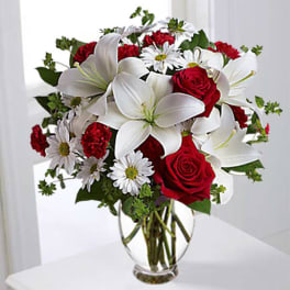 Bouquet of red roses, white lilies, and white daisies in a clear glass vase