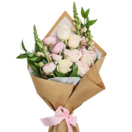 Bouquet of pale pink and white roses wrapped in brown paper with a pink ribbon