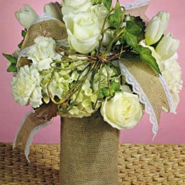 White roses and hydrangeas in a burlap-wrapped vase with lace ribbon