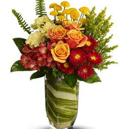 Bouquet of orange roses, red mums, and cream carnations in a glass vase
