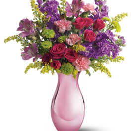 Pink vase holding a mixed bouquet of roses, purple blooms, and carnations