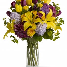 Bouquet of yellow lilies, purple tulips, and hydrangeas in a clear glass vase