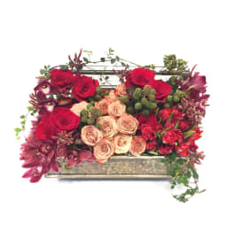 Rectangular floral arrangement with red and blush roses and burgundy orchids in a low container