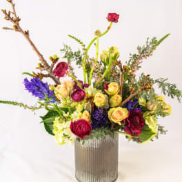 Mixed bouquet of roses, ranunculus, and hyacinth in a ribbed metal vase