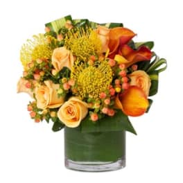 Orange roses and yellow pincushion blooms in a glass vase