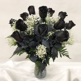 Arrangement of black roses with white filler flowers in a clear glass vase
