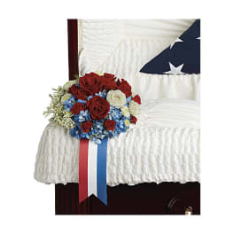 Red, white, and blue floral arrangement on a white-draped casket