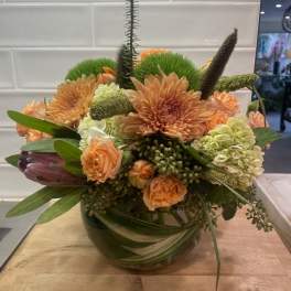 Peach and green floral arrangement in a glass bowl vase