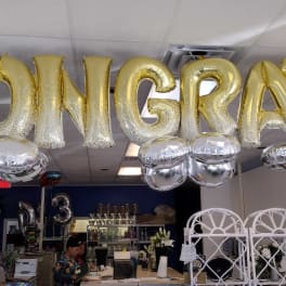 Gold balloon letters spelling CONGRATS hang overhead with silver balloons below.