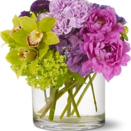 Bouquet of purple and pink flowers with green orchids in a glass vase