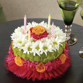 Round floral cake with candles and white daisies on a table