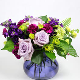 Lavender roses with purple and magenta flowers in a blue glass vase
