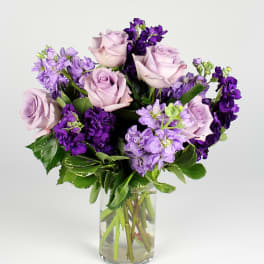 Lavender roses and purple flowers in a clear glass vase