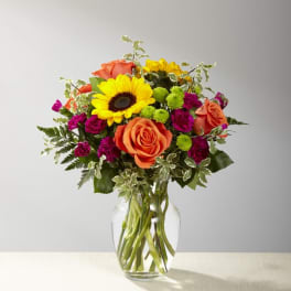 Bouquet of orange roses, sunflowers, and magenta flowers in a glass vase