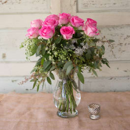 Pink roses arranged in a clear glass vase with greenery