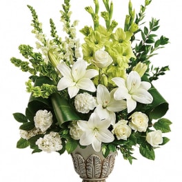 White lilies and roses arranged in a decorative vase with green flowers and foliage