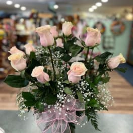 Pink roses arranged in a glass vase with a pink ribbon bow