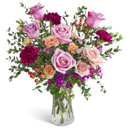 Tall arrangement of pink roses, peach carnations, and magenta blooms in a clear glass vase