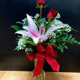 Red roses and pink lilies in a clear glass vase with a red bow