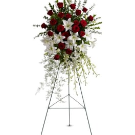 Tall standing spray of red roses with white lilies and orchids displayed on a metal easel.