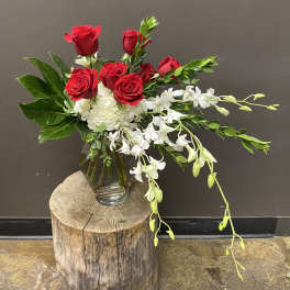 Red roses and white orchids in a glass vase on a wood stump